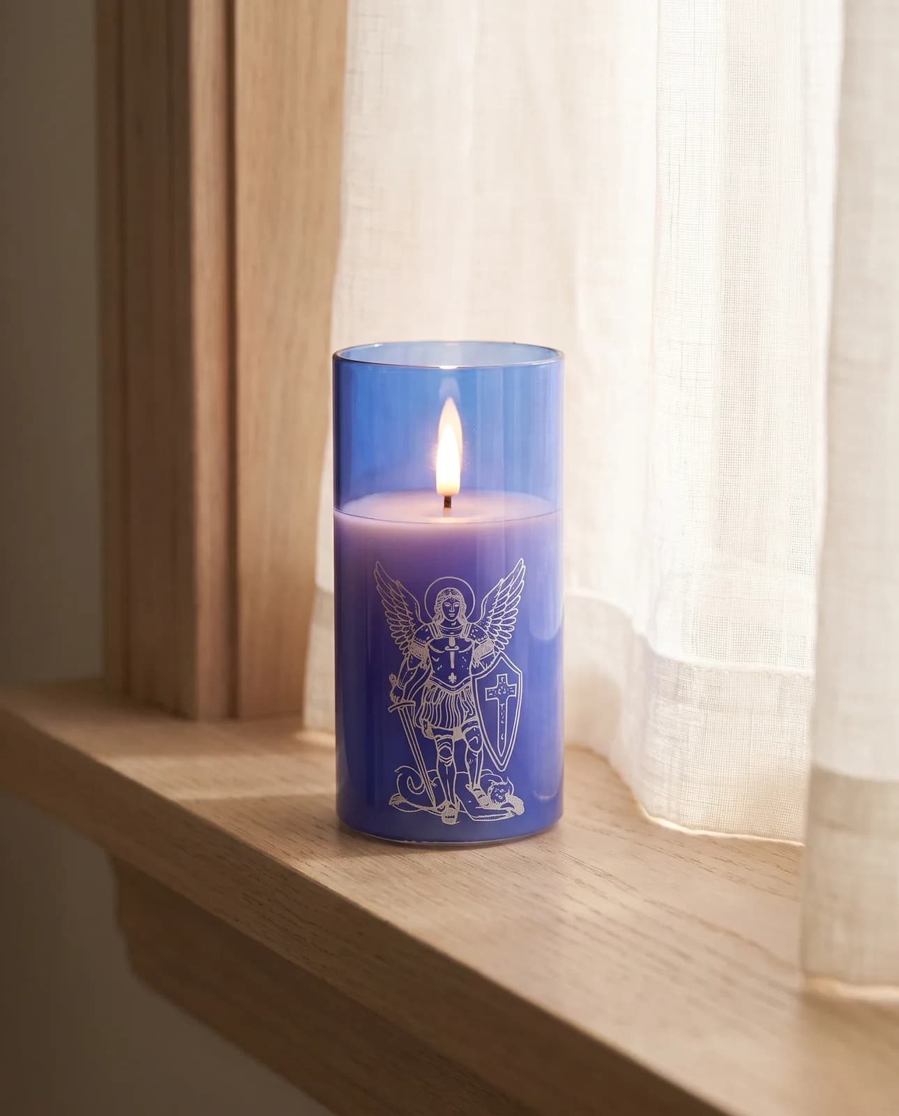 St. Michael candle in blue glass with a white print, lit in morning light