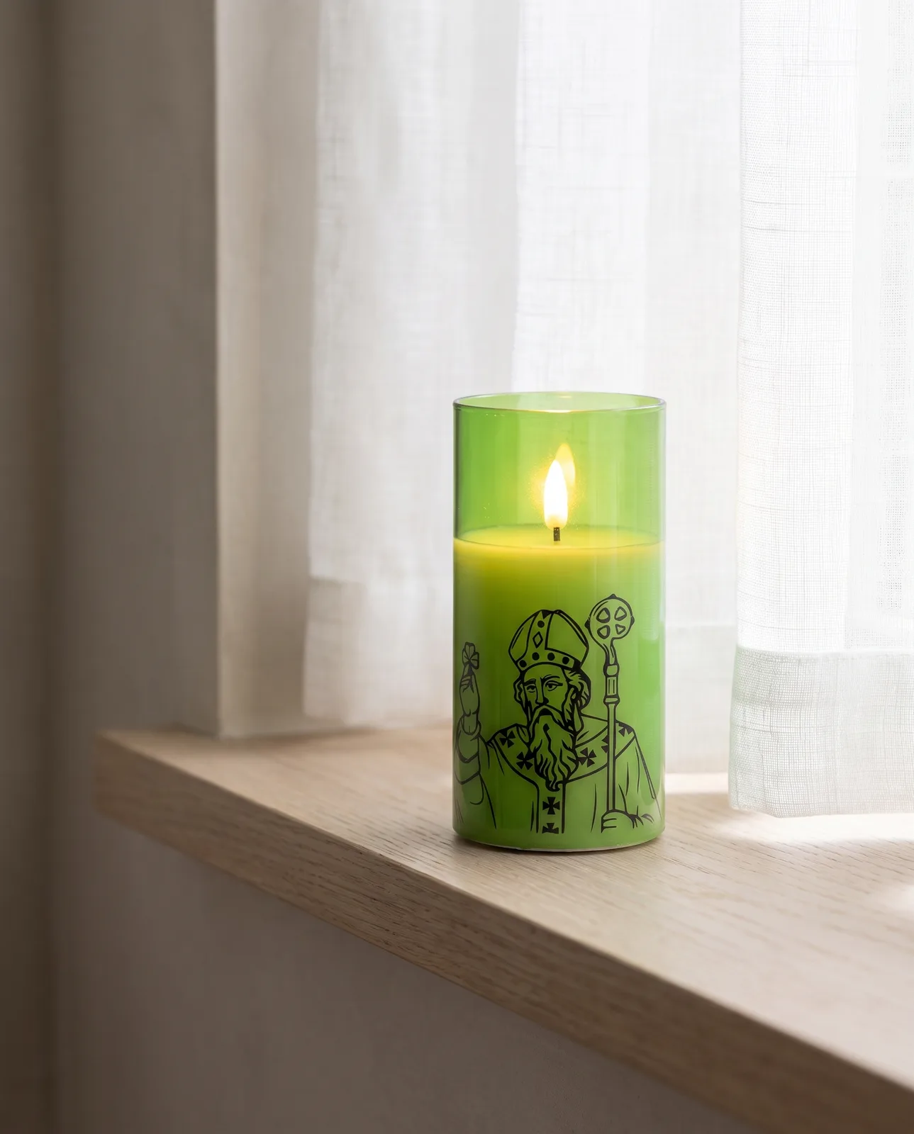 St. Patrick candle in green glass with a black print, lit in morning light