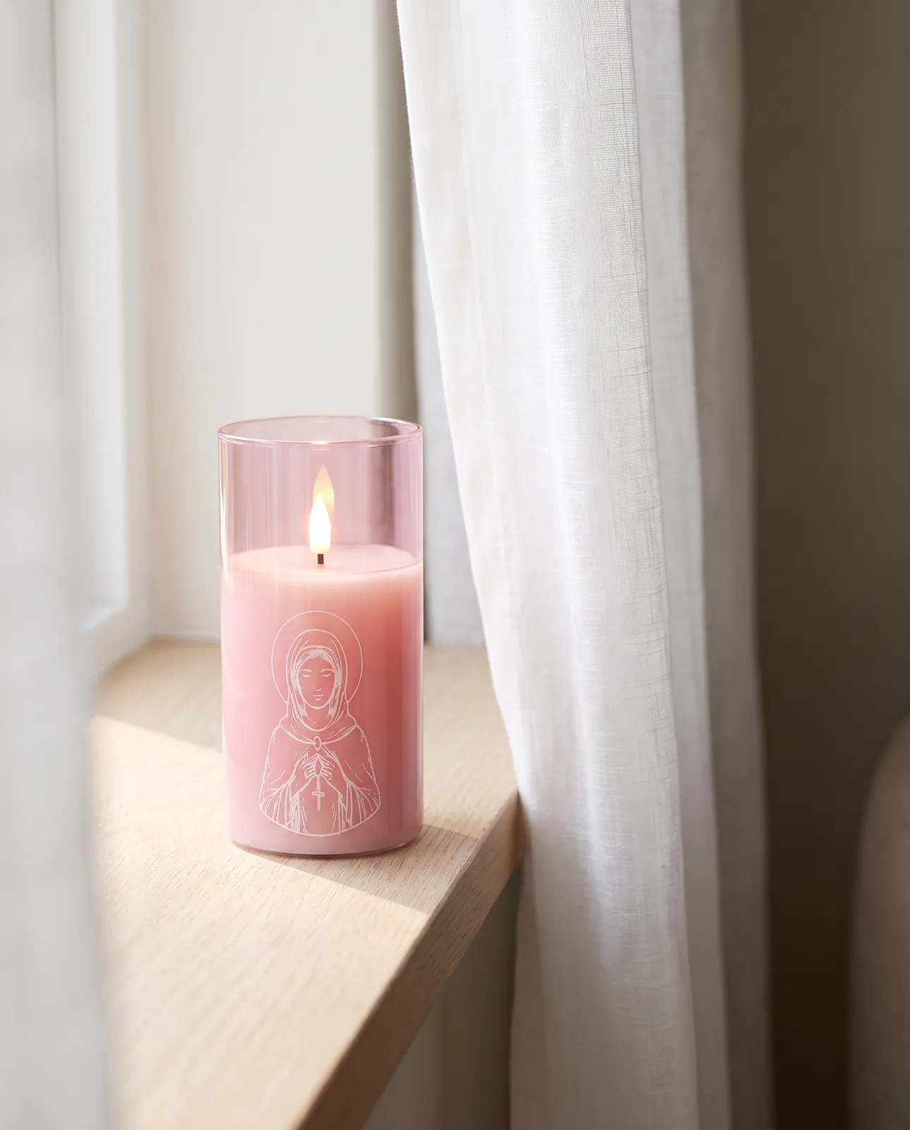 St. Agatha candle in pink glass with a white print, lit in morning light