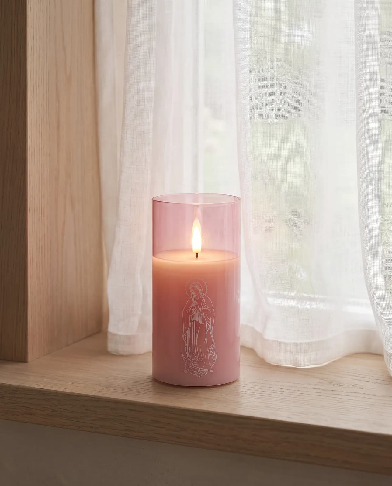 St. Mary candle in pink glass with a white print, lit in morning light