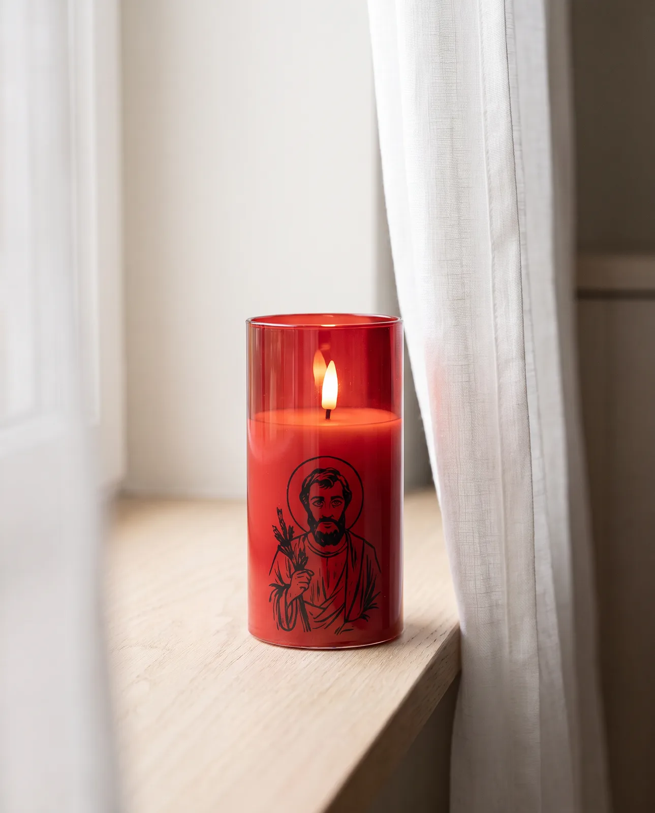St. Joseph candle in red glass with a black print, lit in morning light