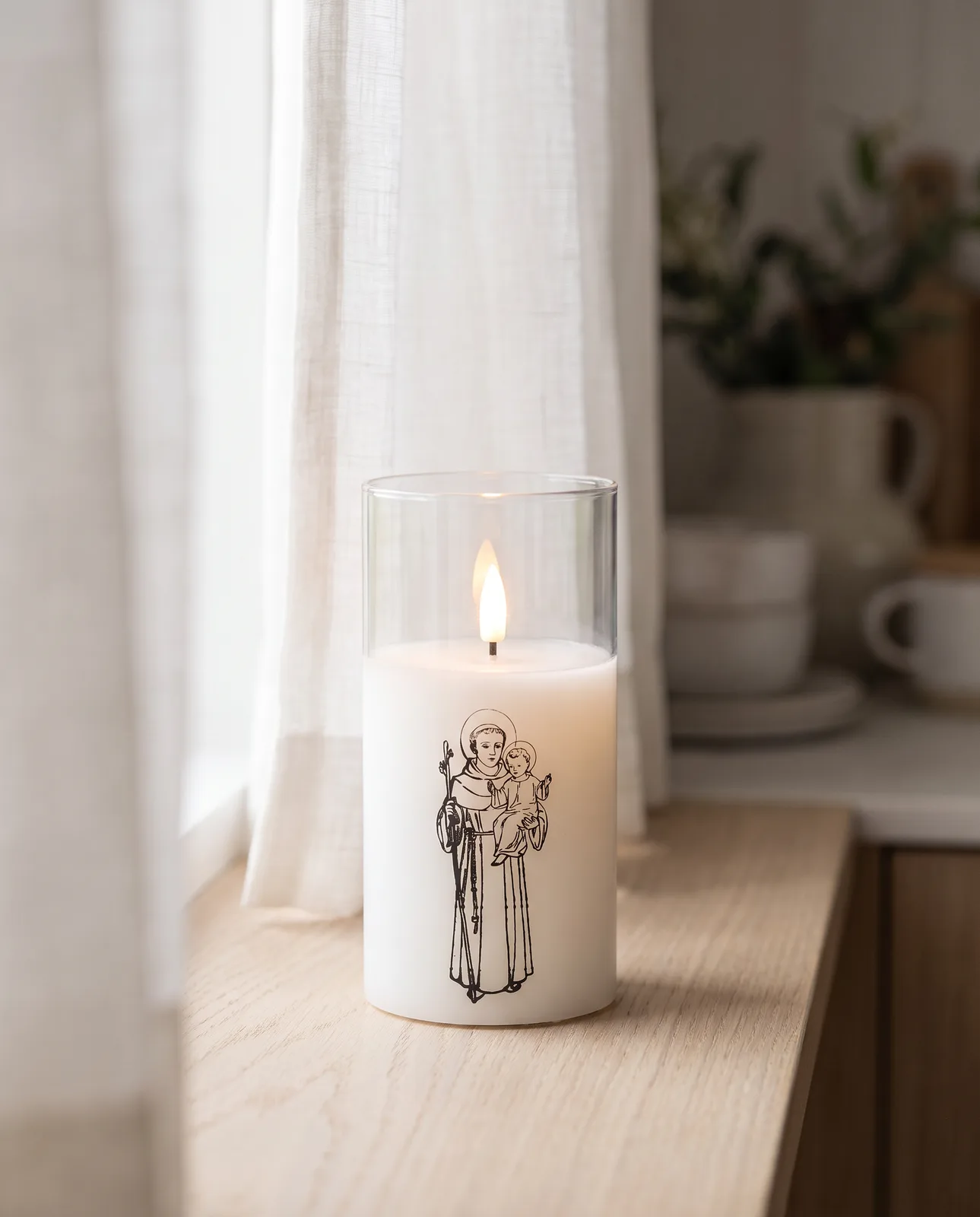 St. Anthony candle in white glass with a black print, lit in morning light